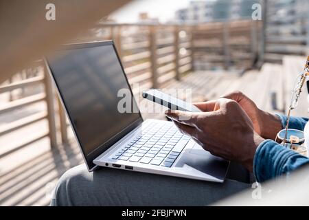 Mann mit Handy über Laptop an der Promenade Stockfoto