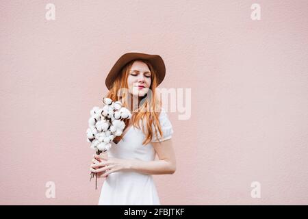Junge Frau mit geschlossenen Augen und einem Haufen Baumwollpflanze Vor einer rosa Wand Stockfoto
