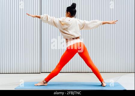 Weibliche Sportlerin, die in Kriegerposition vor der Wand steht Stockfoto