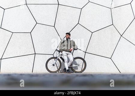 Junger Mann lehnt sich auf das Fahrrad, während er wegschaut Stockfoto