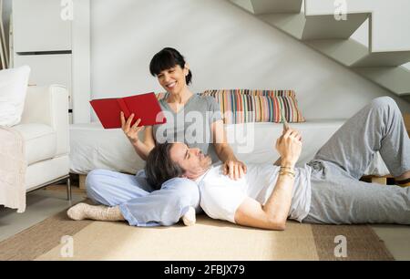 Mann mit Smartphone, der auf dem Schoß der Frau liegt und ein Foto hält Album, während Sie zu Hause sitzen Stockfoto