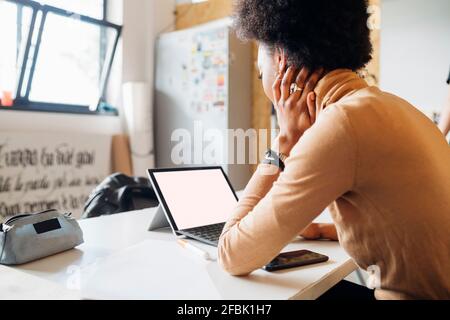 Junge Afrikanerin mit Laptop, während sie am Tisch sitzt studio Stockfoto