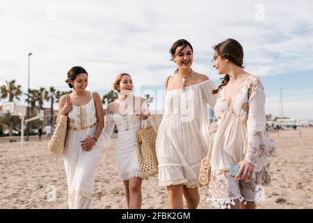 Junge Freunde in weißen Kleidern lächeln beim Spaziergang am Strand Stockfoto