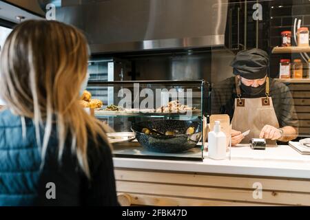 Männliche Kassiererin mit Kreditkartenlesegerät, während weibliche Kundin Warten im Restaurant Stockfoto