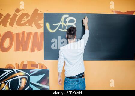 Männlicher Künstler sprüht Farbe mit Aerosoldose auf schwarzen Karton Im Studio Stockfoto