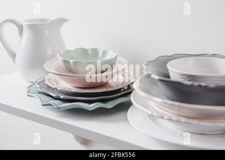 Stapel von sauberen verschiedenen Form Größe und Farbe vintage Stil Geschirr Teller in der Küche zu Hause Regal. Pastellfarben, weißer, minimaler Hintergrund. Stockfoto