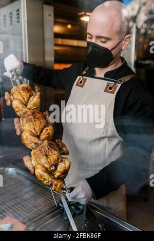 Der Chefkoch hält gegrilltes Hähnchen Tandoori durch das Glas hinein gesehen Küche während einer Pandemie Stockfoto