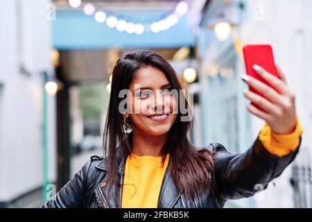 Schöne Frau lächelt, während sie Selfie auf dem Handy in Stadt Stockfoto