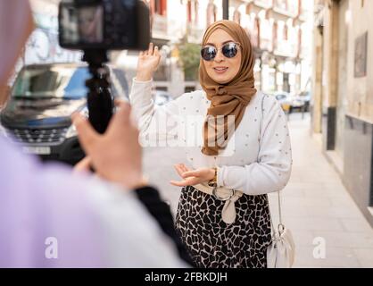 Junge Frau mit Sonnenbrillen gestikuliert beim Vlogging in der Stadt Stockfoto