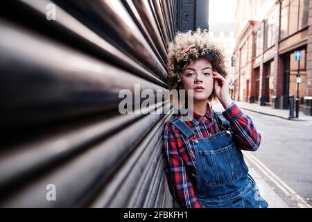 Junge Frau mit der Hand im Haar, die auf Wellblech gelehnt ist Stockfoto