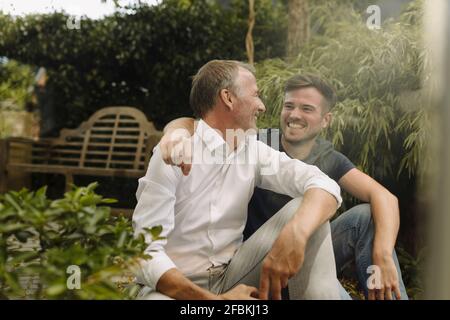 Lächelnder Sohn und Vater schauten einander an, während sie saßen Im Hinterhof Stockfoto
