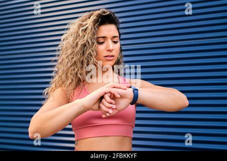 Wunderschöne Sportlerin, die die Zeit auf der Armbanduhr an der blauen Wand überprüft Stockfoto