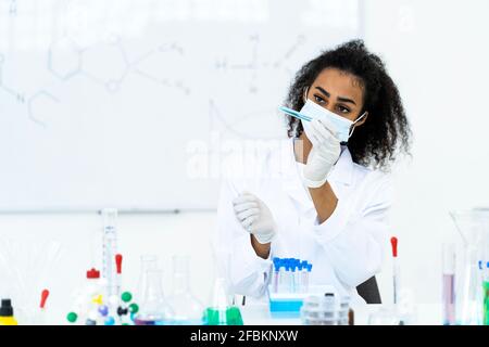 Forscherin analysiert Flüssigkeit im Reagenzglas im Labor während COVID-19 Stockfoto