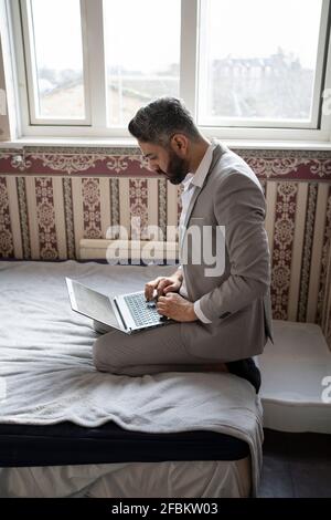 Männlicher Unternehmer mit Laptop, während er zu Hause auf dem Bett sitzt Stockfoto