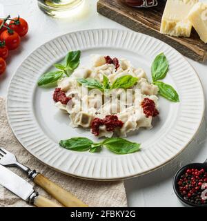 Appetitliche Ravioli mit Tomatensauce, Käse und Basilikum mit Basilikumparmesan und Tomaten auf weißem Teller, auf weißem Hintergrund Stockfoto