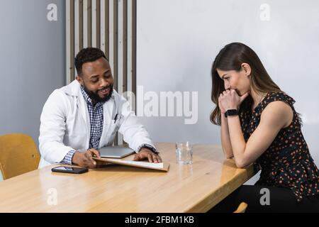Männlicher Arzt, der junge weibliche Patientin am Schreibtisch in der Klinik berät Stockfoto