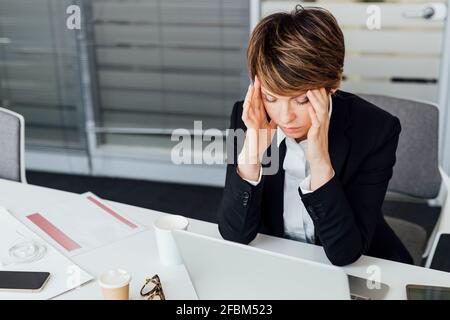 Überarbeitete Geschäftsfrau, die im Büro am Schreibtisch sitzt Stockfoto