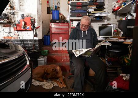 Älterer männlicher Automechaniker, der Zeitung liest, während er in der Garage sitzt Stockfoto