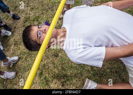 Miami Florida, Tropical Park Drug Free Youth in Town DFYIT, Teenager-Student Anti-Suchtgruppe Picknick, Hispanic Boy Limbo Contest lehnte Anstrengung unter Bar Stockfoto