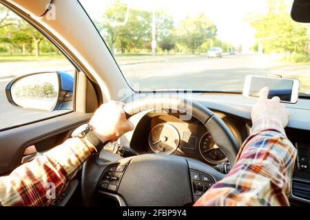 Junger Mann Hand auf Lenkrad fahren Auto berühren Smartphone mit schwarzem Bildschirm. Armaturenbrett, Halterung für Telefonhalterung. Männlicher Hipster fährt Auto, Stockfoto