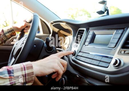 Junger Mann im karierten Hipster-Hemd, der Knöpfe auf dem Auto-Multimedia-Panel drückt und den Drehknopf des Radiosenders schaltet. Nahaufnahme der männlichen Hand am Fahrzeug Stockfoto