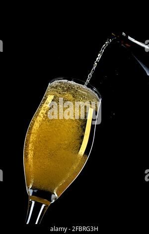 Ein Bier, das in ein Glas auf schwarzem Hintergrund gegossen wird. Stockfoto