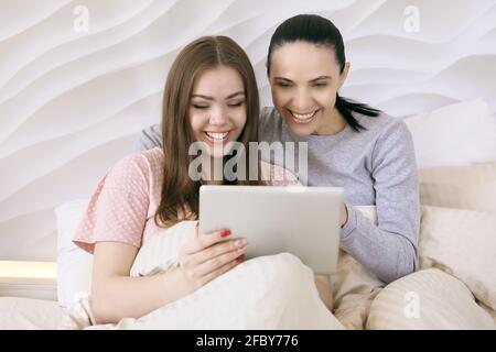 Mutter mit ihrer Tochter im Teenageralter, die sich im Bett einen Film auf dem Tablet-pc-Bildschirm ansieht. Stockfoto