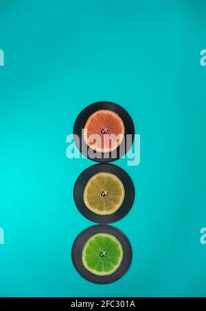 Ampeln aus Früchten und LP-Schallplatten. Türkisfarbener Hintergrund. Zitrone, Limette, Grapefruit. Minimales Verkehrskonzept. Stockfoto