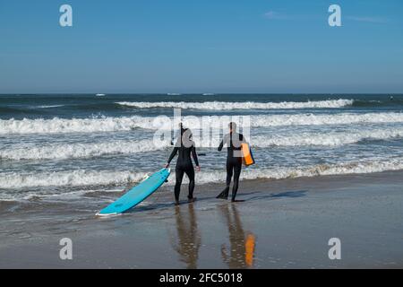 Surf-Ausflug, Paar geht zum Surfen und Bodyboard üben, am Strand spazieren gehen, Surfschulen Aktivitäten. Surf-Lifestyle. Meereswellen. Stockfoto