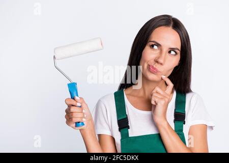 Foto von Dame halten Walze Finger Kinn aussehen leeren Raum Denken Sie tragen grün insgesamt isoliert weißen Hintergrund Stockfoto