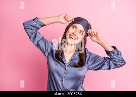 Foto-Porträt von verträumten Mädchen berühren Schlafmaske mit zwei Hände, die isoliert auf einem pastellrosa Hintergrund nach oben schauen Stockfoto