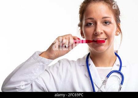 Krankenschwester oder Zahnarzt mit Laborkittel und Stethoskop, Demonstration Zähneputzen mit einer roten Plastikzahnbürste in einem Konzept der Zahnhygiene Stockfoto