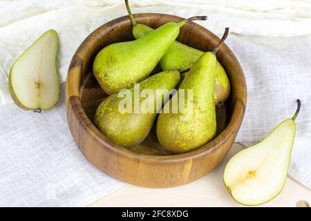 Frische grüne Bio-Birnen reifen in der runden Holzschale auf hellem Hintergrund in der Küche. Stockfoto