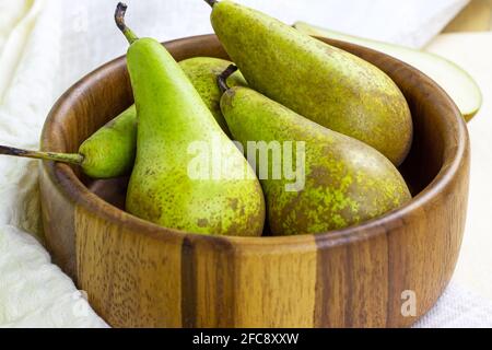 Frische grüne Bio-Birnen reifen in der runden Holzschale auf hellem Hintergrund in der Küche. Stockfoto