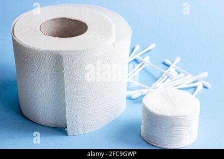 Weiße weiche Wattepads und -Sticks für Hygiene und Gesundheitswesen sowie Toilettenpapierrolle auf hellblauem Hintergrund. Stockfoto