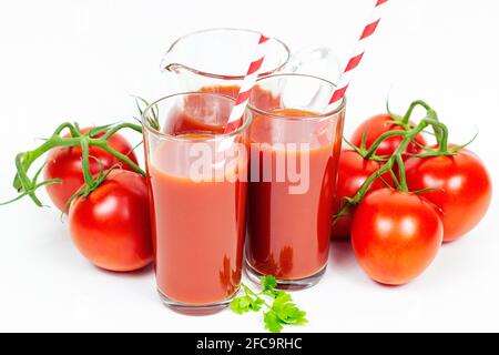 Frischer natürlicher Bio-Tomatensaft in den Gläsern mit Papierstrohhalmen und Tomaten auf weißem Hintergrund. Stockfoto