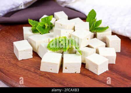 Rohe vegetarische Tofu-Würfel aus biologischem Anbau mit frischer Minze auf Holzgrund. Stockfoto