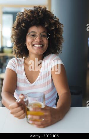 Porträt einer Frau mit gemischter Rasse, die am Tisch sitzt und lächelt Bier Stockfoto