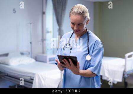 Lächelnde kaukasische Ärztin im Krankenhaus mit Peelings und Stethoskop Mit Tablet Stockfoto