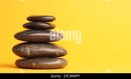Haufen von fünf dunklen Massagesteinen auf gelbem Hintergrund Mit Platz für Text Stockfoto