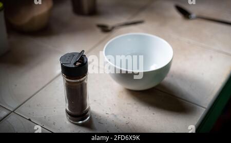 Sofortiges Kaffeepulver in einer kleinen durchsichtigen Glasflasche und einer weißen Schüssel, um den Kaffee in den Schaum zu schlagen, Zeit für die Zubereitung von Dalgona Kaffee in der heimischen Küche. Stockfoto