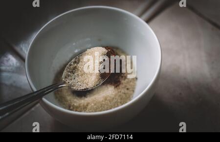 Messung von Zucker und Instant-Kaffeepulver durch Esslöffel in eine weiße Schüssel. Vorbereitung von Zutaten für die Herstellung von Dalgona Kaffee Schaum. Ein Löffel Zucker a Stockfoto