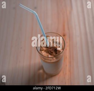 Trendiges koreanisches Getränk Dalgona Kaffee und ein Stroh in einem Glas auf einer Tischplatte, oben Nahaufnahme. Hergestellt mit Instant-Kaffee und frischer Milch mit hinzugefügt Stockfoto