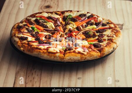 Hausgemachte gebackene Hühnerkäse-Pizza auf einem Teller auf einer Holzplatte, in Scheiben geschnitten und bereit, in heißen Stücken zu servieren. Stockfoto