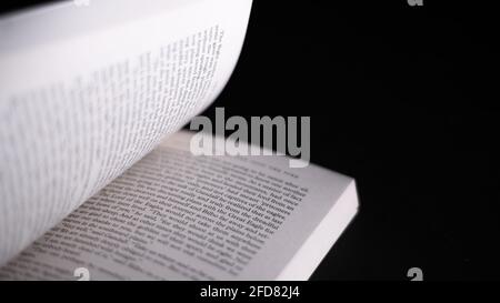 Scrollende Seiten in einem englischen Romanbuch. Isoliertes offenes Buch auf dunkelschwarzem Hintergrund. Lesekonzept macht einen vollen Mann. Stockfoto