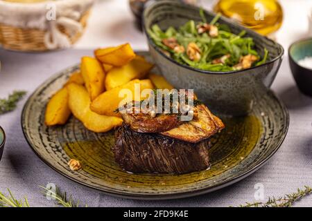 Steak mit gegrillter Entenleber serviert mit Kartoffelkeilen und Aragula Stockfoto