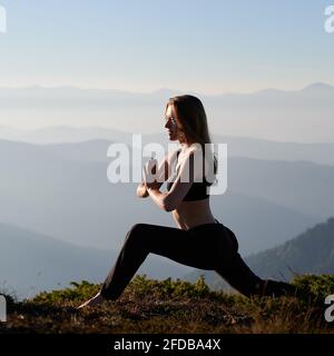 Sportlich schlanke Frau in schwarzer Sportbekleidung, die Yoga-Übungen in der Natur mit schöner Landschaft macht. Konzept der Entspannung auf der Natur. Stockfoto