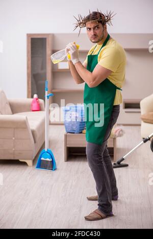 Junger männlicher Auftragnehmer, der auf dem Kopf einen stacheligen Kranz trägt und Hausarbeit leistet Stockfoto