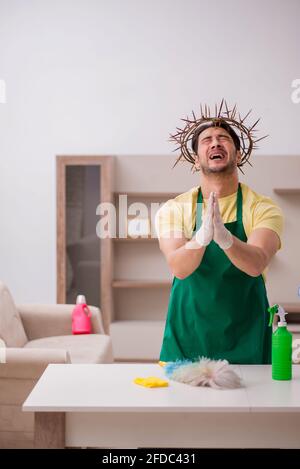 Junger männlicher Auftragnehmer, der auf dem Kopf einen stacheligen Kranz trägt und Hausarbeit leistet Stockfoto