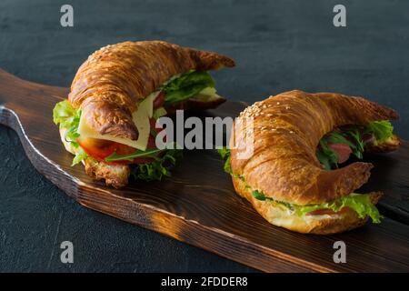 Croissant-Sandwiches mit gesalzenem Lachs auf einem Schreibtisch, serviert mit frischen Salatblättern, Rucola und Gemüse auf schwarzem Hintergrund. Stockfoto